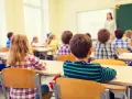 Dzieci siedzą w ławkach podczas lekcji religii w szkole, słuchając nauczycielki stojącej przy tablicy.