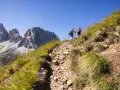 Due escursionisti affrontano un sentiero roccioso sui **cammini in Trentino**, con imponenti vette sullo sfondo.