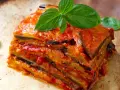 Una fetta di parmigiana di melanzane, stratificata e succulenta, guarnita con basilico fresco.