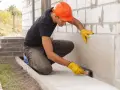 Obrero con casco naranja aplica producto para impermeabilizar pared exterior de bloque de hormigón.