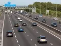Autostrada z ruchem lewostronnym, pełna samochodów i ciężarówek. Znaki drogowe wskazują M1, A405 i M25.