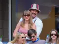 Travis Kelce e Taylor Swift sorridono, lei con un vestito a quadri rossi, lui con un cappello Gucci.