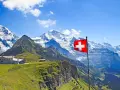 A Swiss flag flies proudly against a backdrop of majestic snow-capped mountains and lush green slopes, showcasing the beautiful places of nature in Switzerland.