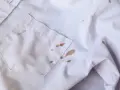 Biała koszula z licznymi brązowymi plamami z błota na kieszeni i rękawie.