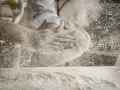 Ręce formują ciasto, a mąka do pizzy unosi się w powietrzu. Idealna do wypieku chrupiącej podstawy.