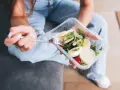 Kobieta je sa widelcem sa sałatką z kurczakiem i jajkiem w plastikowym pojemniku.