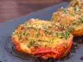 Pomodori gratinati in padella, con croccante panatura alle erbe e formaggio, serviti su una pietra scura.