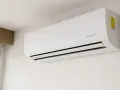 Unidad de aire acondicionado blanca con tecnología inverter, montada en pared blanca, cerca de una ventana.