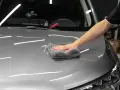 A hand buffs a car's hood with a microfiber cloth, applying a ceramic wax for a deep shine.