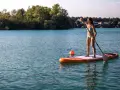 Frau genießt das sub fahren auf einem ruhigen See, umgeben von grünen Bäumen und Häusern.