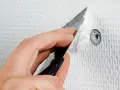 En hand använder en spackel för att spackla hål i en vit vägg.