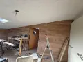 Taket är målat OSB. Rummet är under renovering med träpanel på väggarna, en dörr med runt fönster och byggmaterial utspritt.