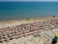 A crowded beach with rows of umbrellas and sunbathers, and people swimming in the blue sea.
