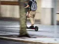 En person på elsparkcykel, med ryggsäck, susar fram på trottoaren. Frågan om får man åka två på elsparkcykel är relevant här.