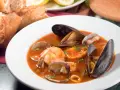 Sopa de mariscos en plato blanco con mejillones, camarones, almejas y pan.