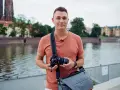 Mężczyzna z aparatem, gotowy na kurs EOS. W tle rzeka i zabytkowe budynki.