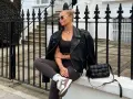 Kobieta w skórzanej kurtce i legginsach, uosobienie stylu athleisure, siedzi na murku przed kamienicą.