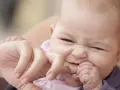 Ein süßes Baby mit einem lustigen Gesichtsausdruck, das gerade versucht, den Finger einer erwachsenen Person zu beißen.