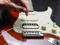 Dłoń naciąga nowe struny w gitarze elektrycznej, przygotowując ją do gry.