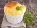 Un soufflé au fromage doré et gonflé, garni de persil frais, dans un ramequin blanc sur une serviette grise.