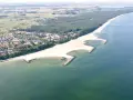 Jarosławiec nad morzem: szeroka, piaszczysta plaża z kamiennymi falochronami, otoczona lasem sosnowym i zabudową letniskową.