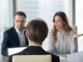 Besprechung mit einem Anwalt über Versicherungsansprüche. Eine Frau gestikuliert, während ein Mann mit Brille und ein Mann im Vordergrund zuhören.