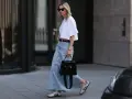 Kobieta w białej bluzce i długiej spódnicy jeansowej, z czarną torebką i sneakersami. Stylowe długa spódnica jeansowa stylizacje.