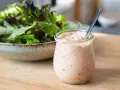 Ein Glas mit Thousand Island Dressing steht neben einer Schüssel Salat. Perfekt für den nächsten Salat!