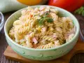 Ein cremiger Nudelsalat mit Erbsen, Mais und Schinkenwürfeln, der an einen herzhaften Fleischsalat erinnert. Garniert mit Petersilie.