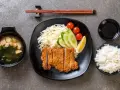 Chrupiące katsu na talerzu z ryżem, zupą miso, warzywami i cytryną. Idealny zestaw do jedzenia pałeczkami.