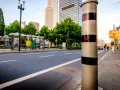 Blitzlicht warnt: Innerorts 17 kmh zu schnell. Ein Blitzer steht am Straßenrand, im Hintergrund Hochhäuser und Bushaltestellen.