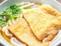 Pyszna zupa z makaronem udon z dwoma kawałkami smażonego tofu i zieloną cebulką.