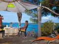 Para na plaży, relaksująca się w namiocie. Mężczyzna obserwuje morze przez lornetkę. To idealne miejsce na naturystyczny camping.