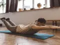 Homme faisant un exercice dos sur un tapis, bras tendus, jambes levées.