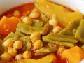 Un plato humeante de olla gitana, con garbanzos tiernos, judías verdes y trozos de calabaza en un rico caldo.