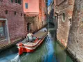 Un uomo guida una barca su un canale stretto a Venezia, circondato da edifici in mattoni. Quanti canali ci sono a Venezia? Molti, come questo!