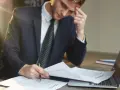 Zestresowany mężczyzna w garniturze analizuje dokumenty, być może dotyczące upadłości firmy.