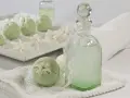 Zielone kule do kąpieli i butelka z płynem, ozdobione kwiatami. W składzie kosmetyków może być tocopherol, znany z właściwości pielęgnacyjnych.