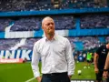 Trener w białej koszuli na tle trybun pełnych kibiców podczas meczu Widzew Łódź – Lech Poznań.