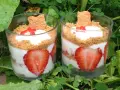 Deux verrines de tiramisu fraises spéculoos, garnies de crème, fraises fraîches et biscuits spéculoos, posées sur un lit de verdure.
