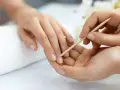 Delikatne odsuwanie skórek drewnianym patyczkiem podczas manicure biologicznego. Dłonie zadbane i naturalne.