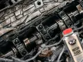 Silnik z widocznymi elementami rozrządu, pokryty czarnym osadem. Obok butelka płukanki K2 Motor Flush, która pomoże rozwiązać problem niskie ciśnienie oleju na rozgrzanym silniku.