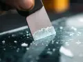 A scraper is used to remove adhesive from acrylic, leaving behind small white fragments.