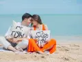 Para zakochanych na plaży z poduszkami "Mr. Right" i "Mrs. Always Right". Ich uśmiechy i bliskość symbolizują idealny **kompromis w związku**.