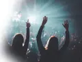 Zwei Frauen jubeln mit erhobenen Armen bei einem Konzert. Ein Lichtstrahl durchbricht die Dunkelheit, perfekt für einen **single release**.