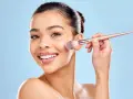 Une femme souriante utilise un pinceau pour appliquer du correcteur maquillage sur sa joue.