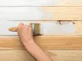 Ręka maluje białą farbą drewnianą boazerię, pokazując, jak odnowić starą boazerię.