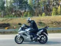 Motocyklista w kasku jedzie na srebrnym Honda VFR 800 wzdłuż leśnej drogi.