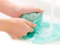 Hände waschen ein türkises Tuch im Waschbecken, um Fettflecken zu entfernen. Wasser sprudelt und schäumt.