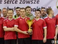 Drużyna w czerwonych koszulkach świętuje zwycięstwo z pucharem. W centrum stoi Andrzej Zaborowski, dumny z sukcesu.
